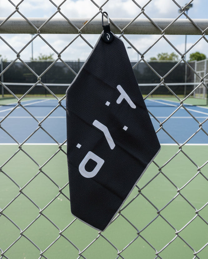Black towel with 'AYP' logo hanging on a chain-link fence with a tennis court in the background