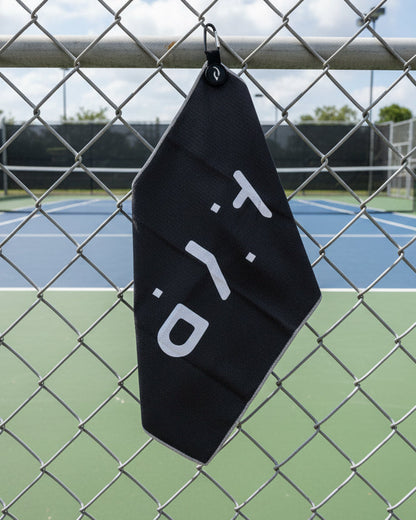 Black towel with 'AYP' logo hanging on a chain-link fence with a tennis court in the background