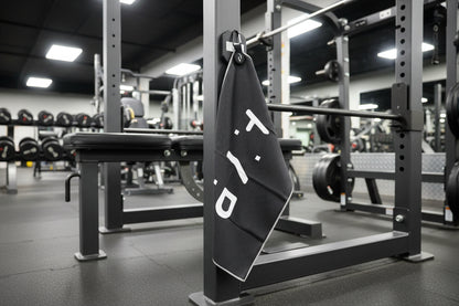 Gym towel with 'AYP' branding hanging on a barbell rack in a gym.